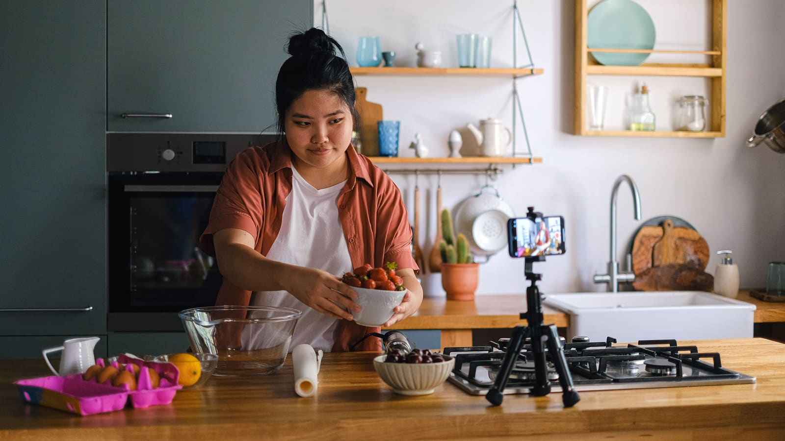 A creator recording a kitchen video on a phone and tripod, the back-to-uploading moment a channel revival starts with