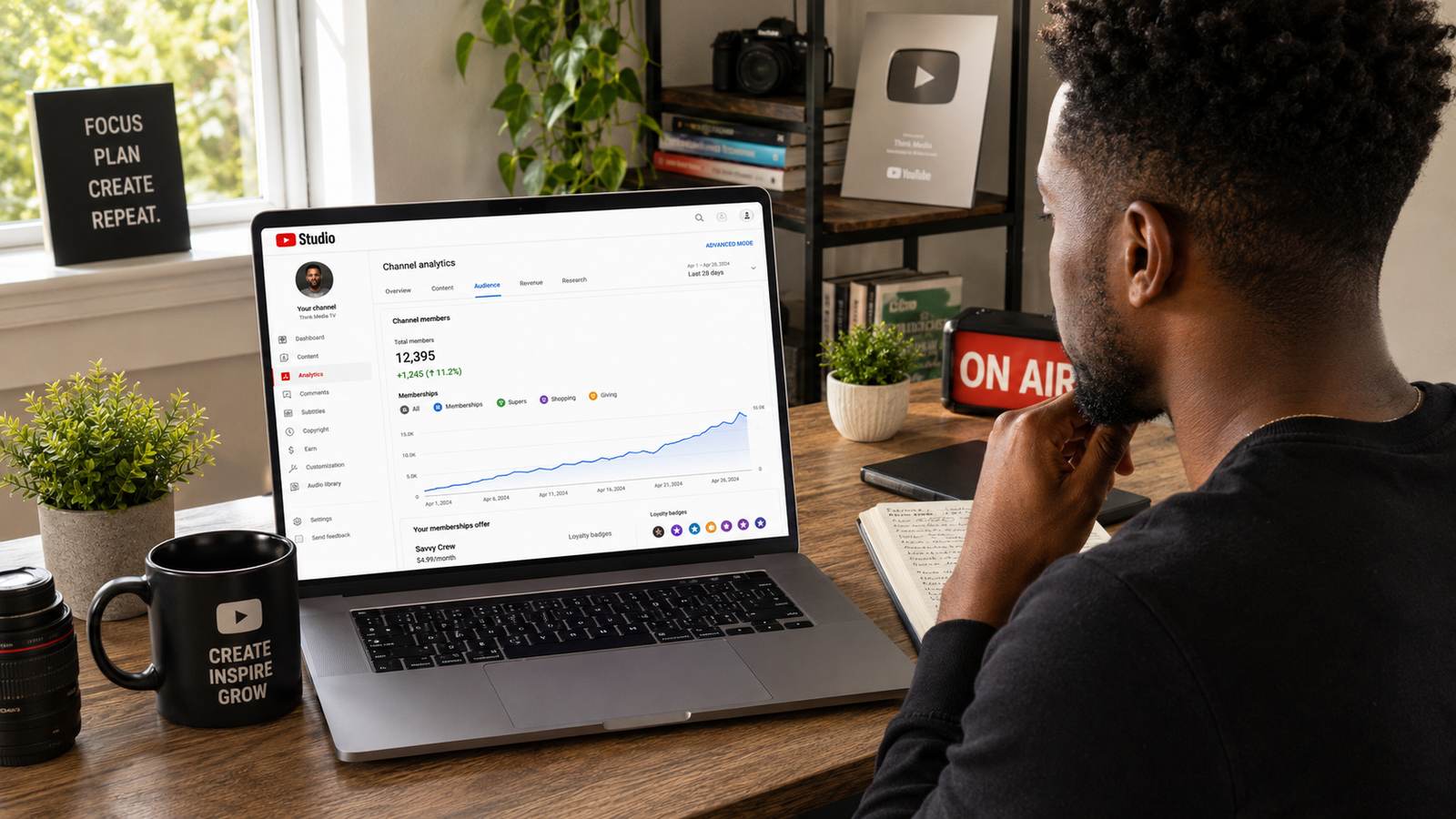 A creator looking over his shoulder at a laptop showing YouTube Studio channel membership analytics, with a rising members graph and pricing tier visible on screen, in a home studio with plants and camera gear in the background